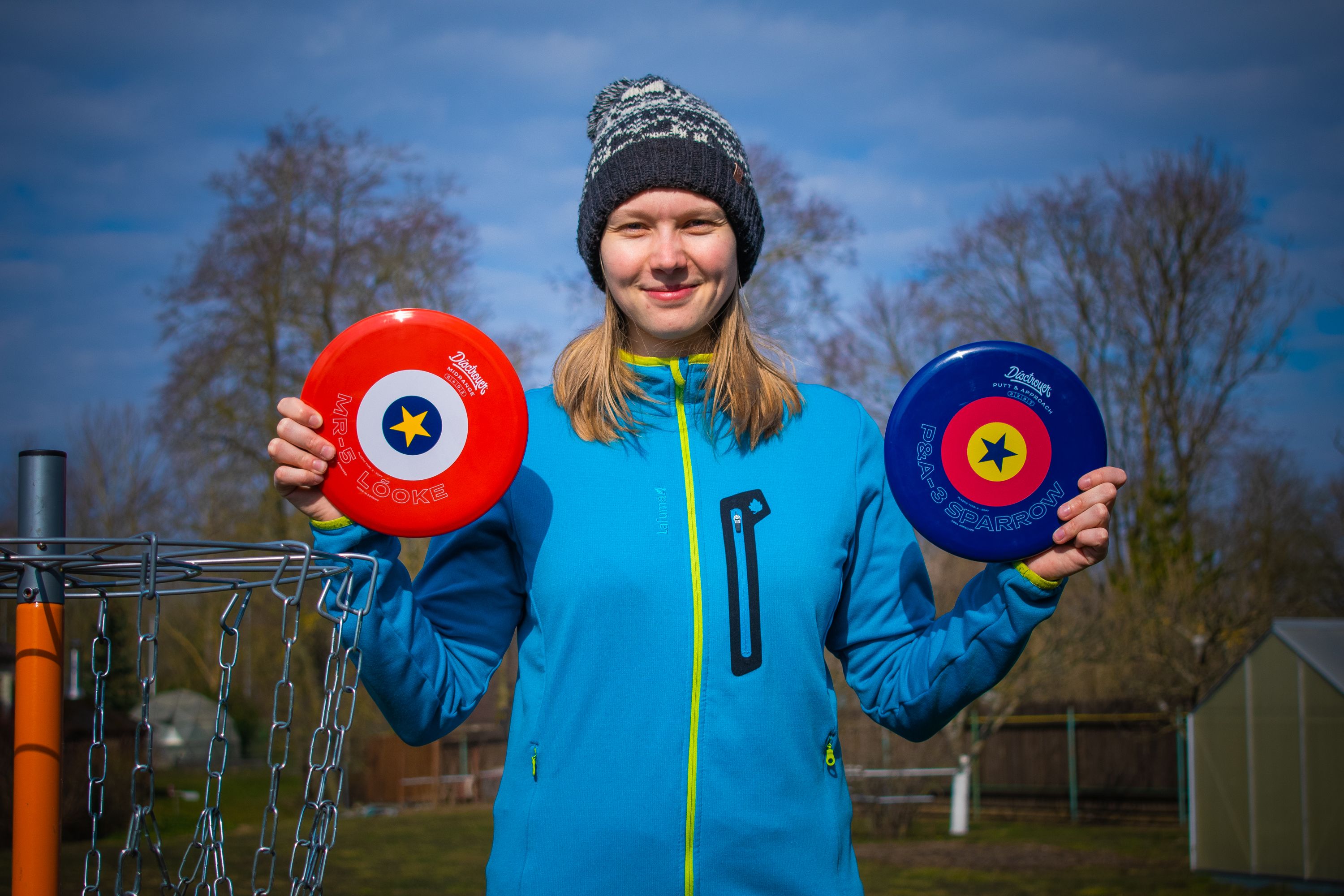 Young woman holding frisbee golf discs, enjoying a sunny day in an Estonian park.