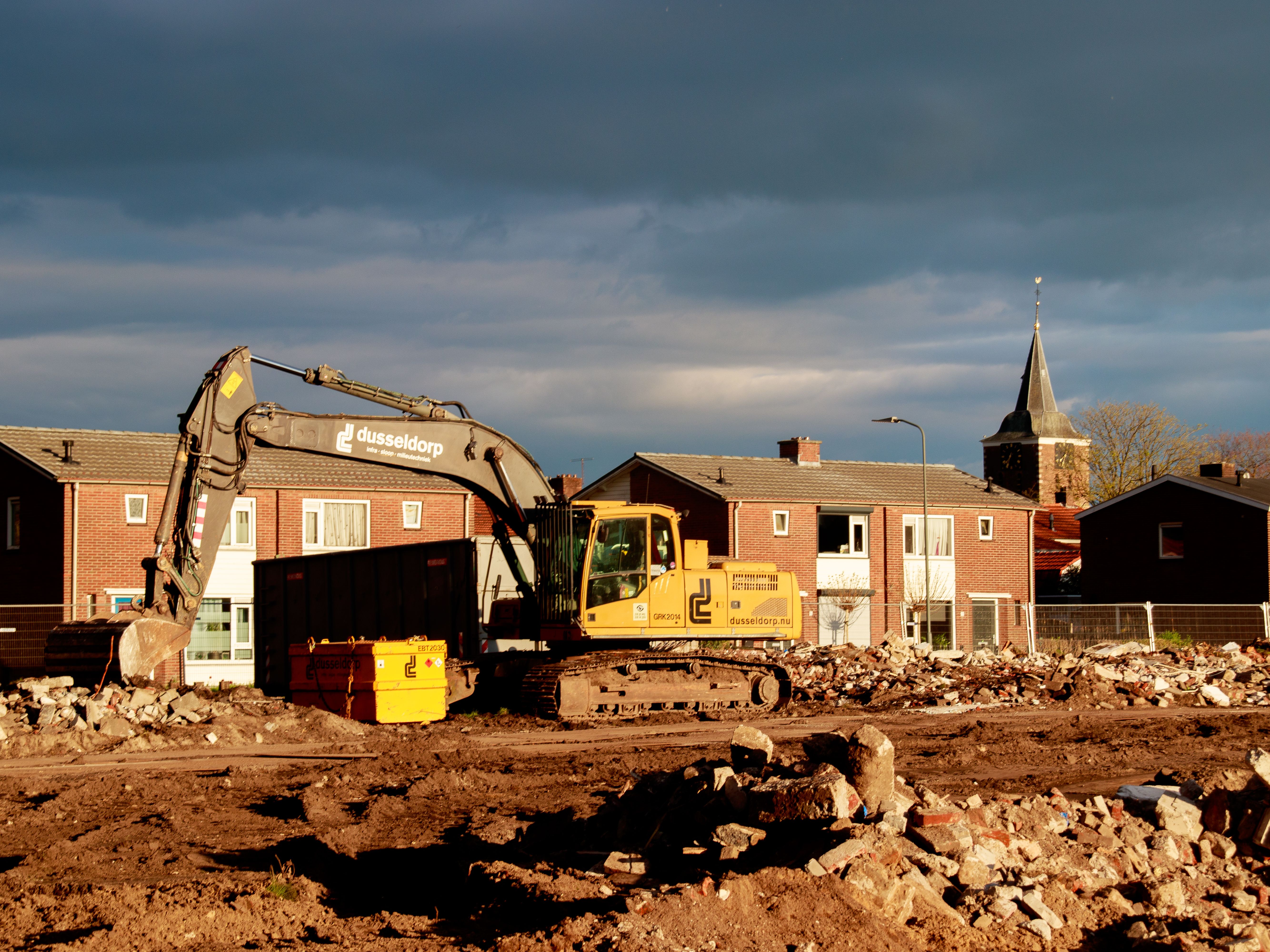 Excavator at a construction site near residential houses under a dramatic sky