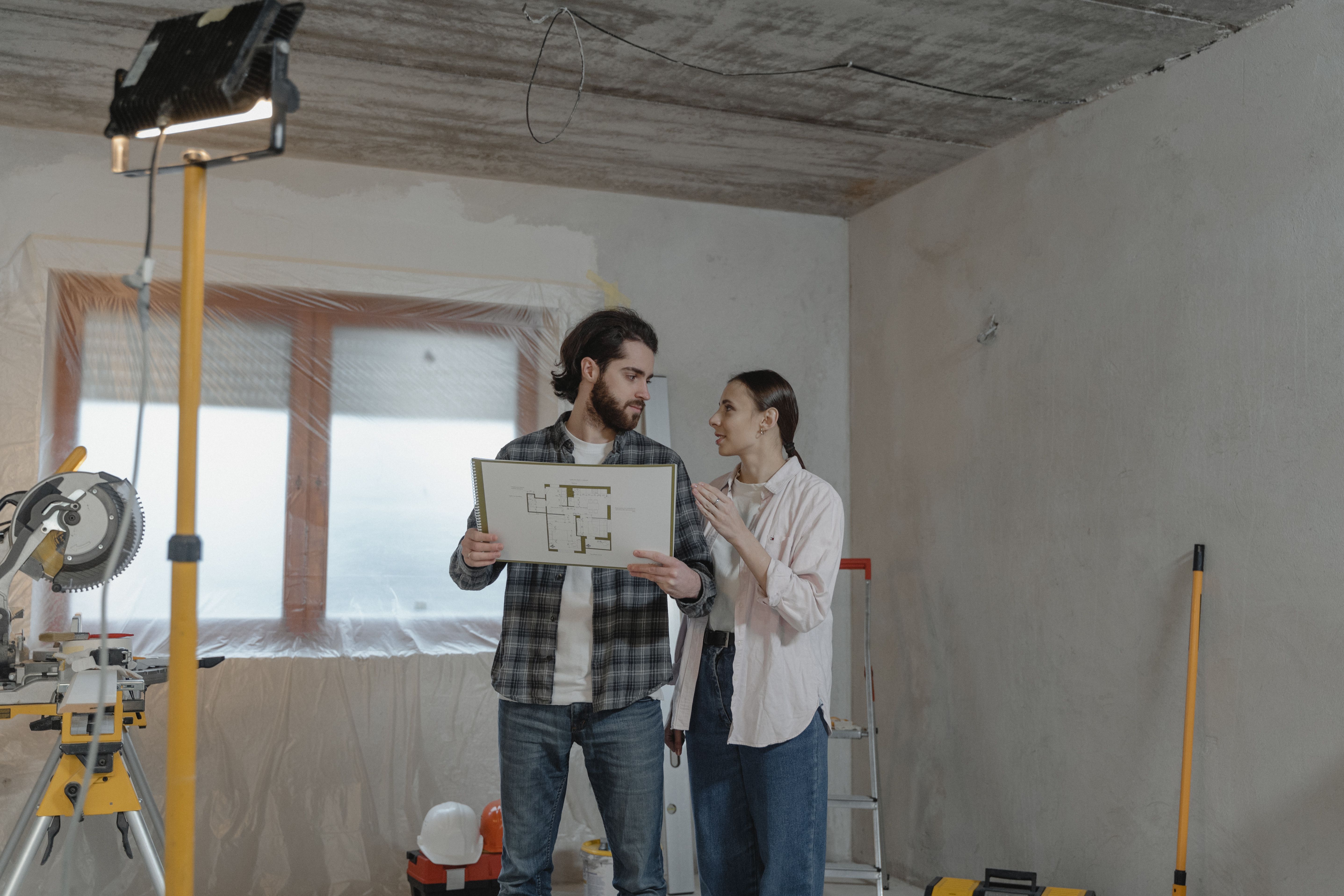 A couple reviews a blueprint in a partially renovated room while planning home improvements