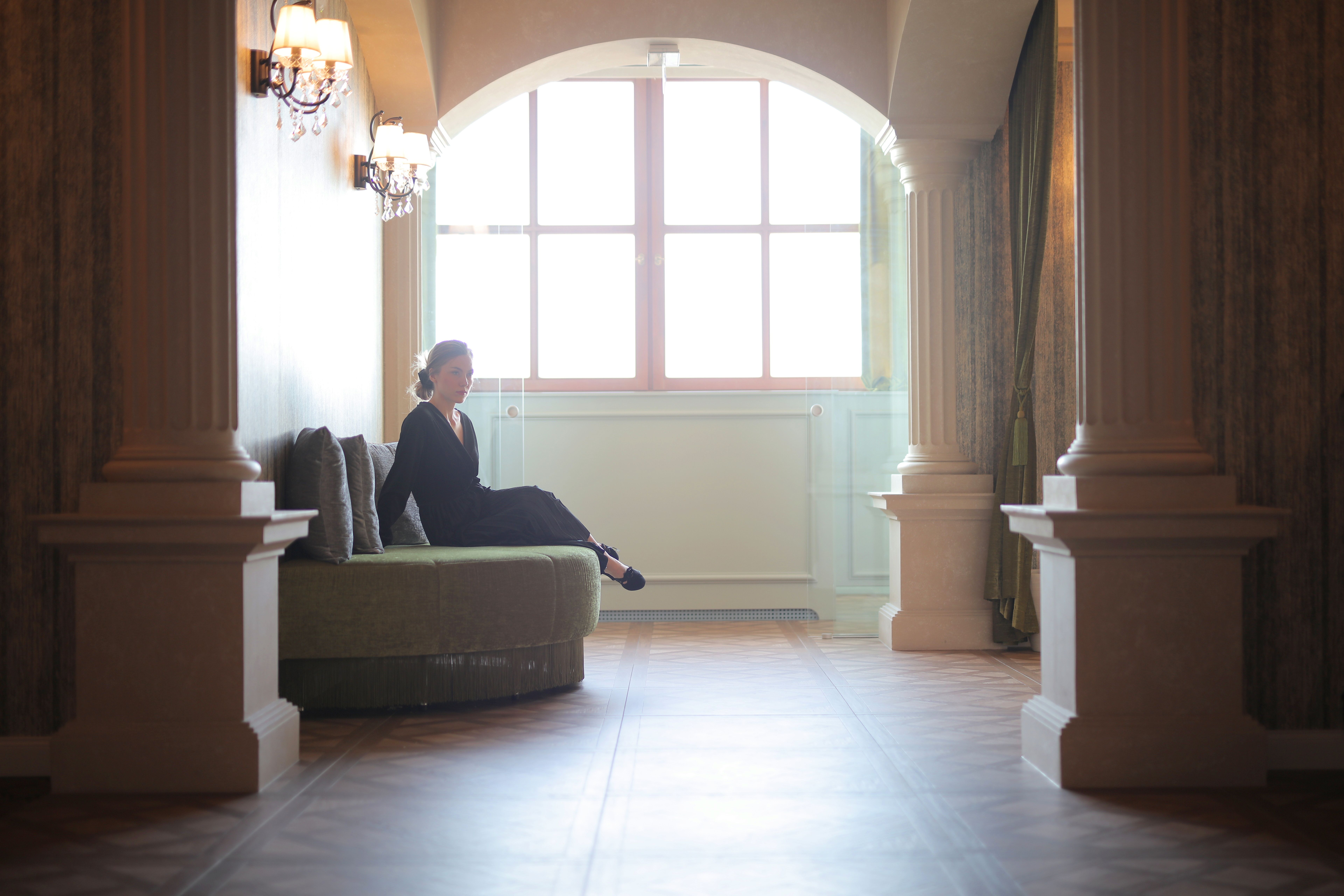 Elegant woman in a black dress seated discreetly in a classic hotel lobby with architectural columns