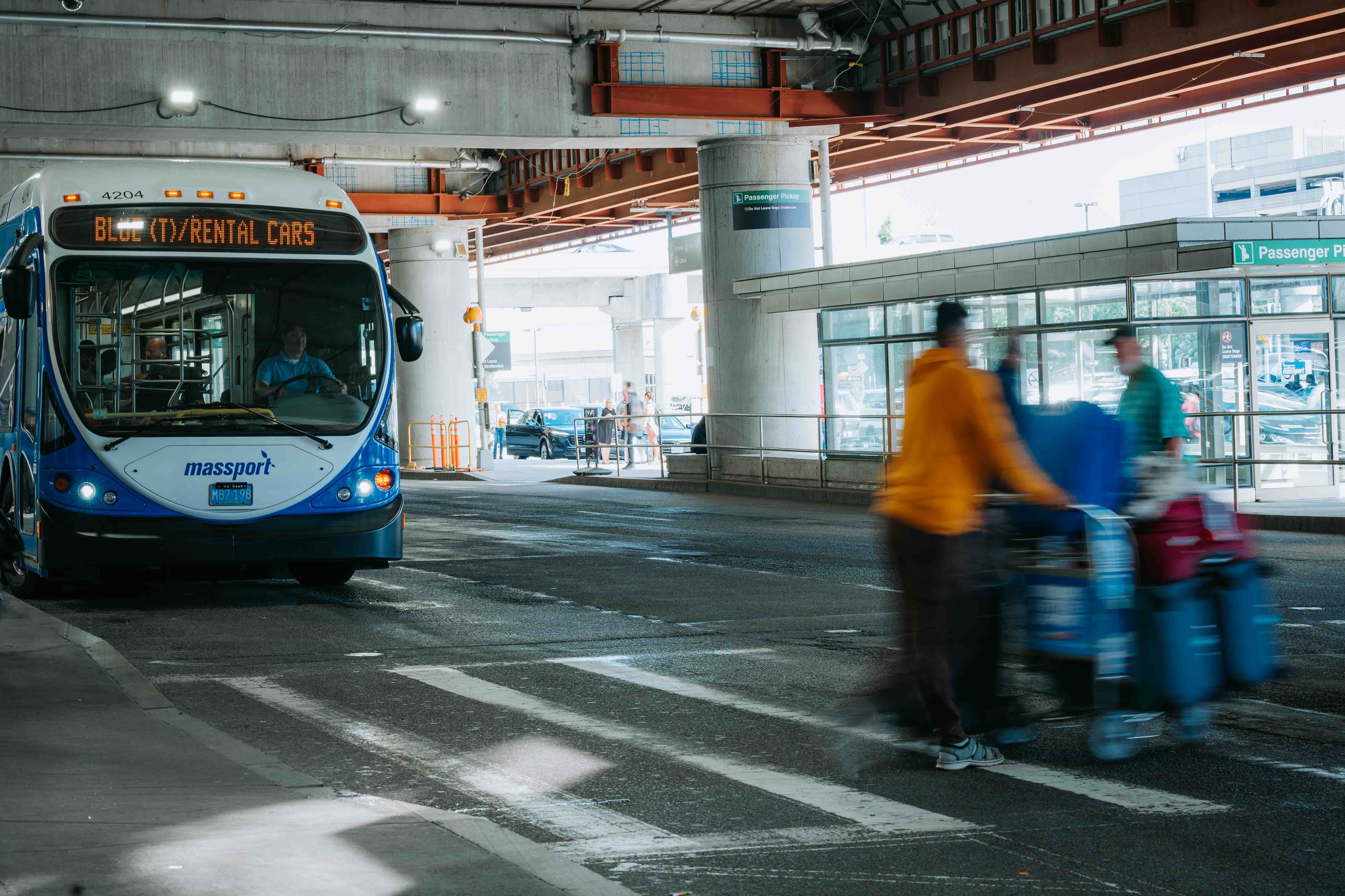 Travelers outside an airport terminal beside a shuttle bus serving rental car passengers.