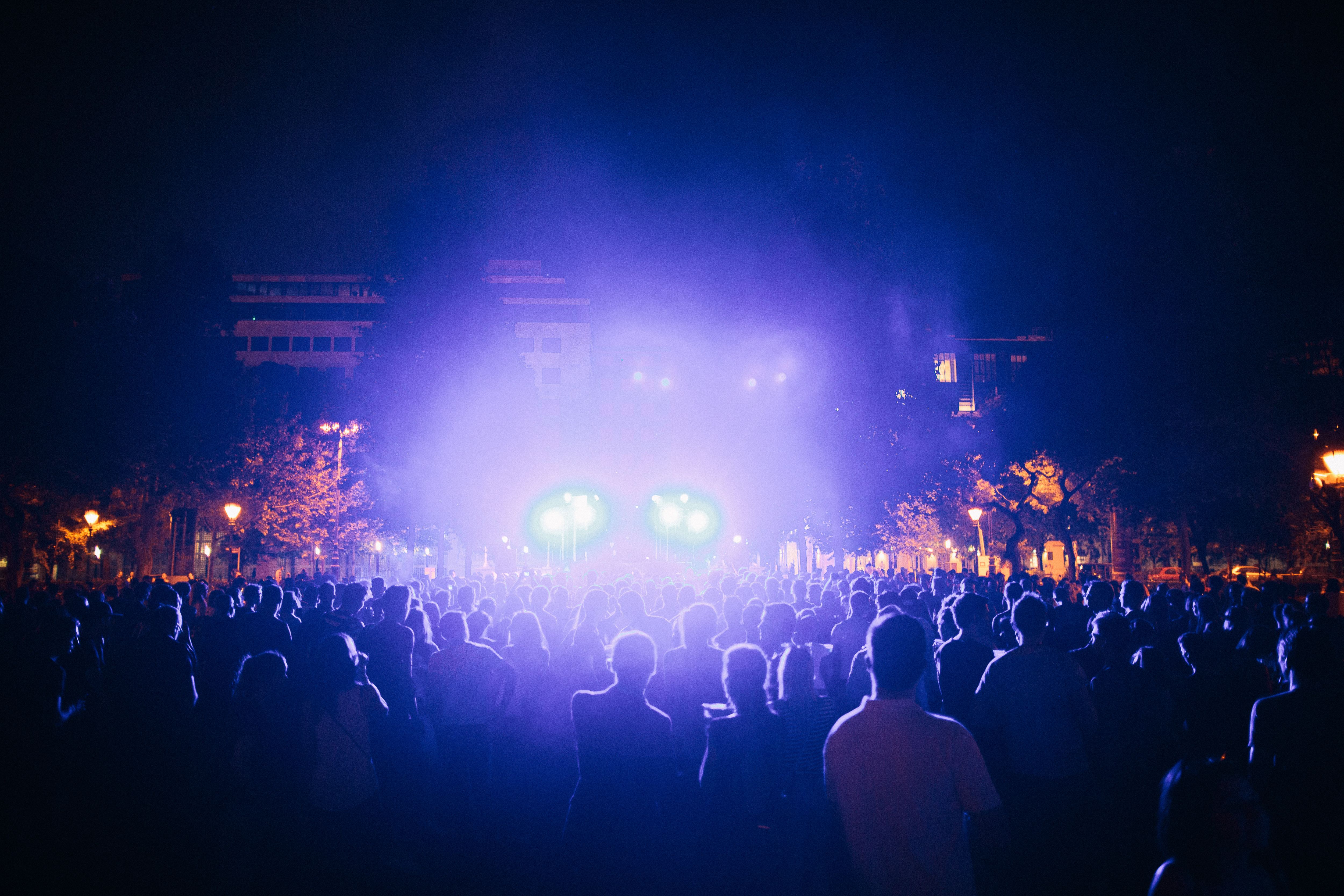 Outdoor concert at night with colorful stage lights and an engaged audience.