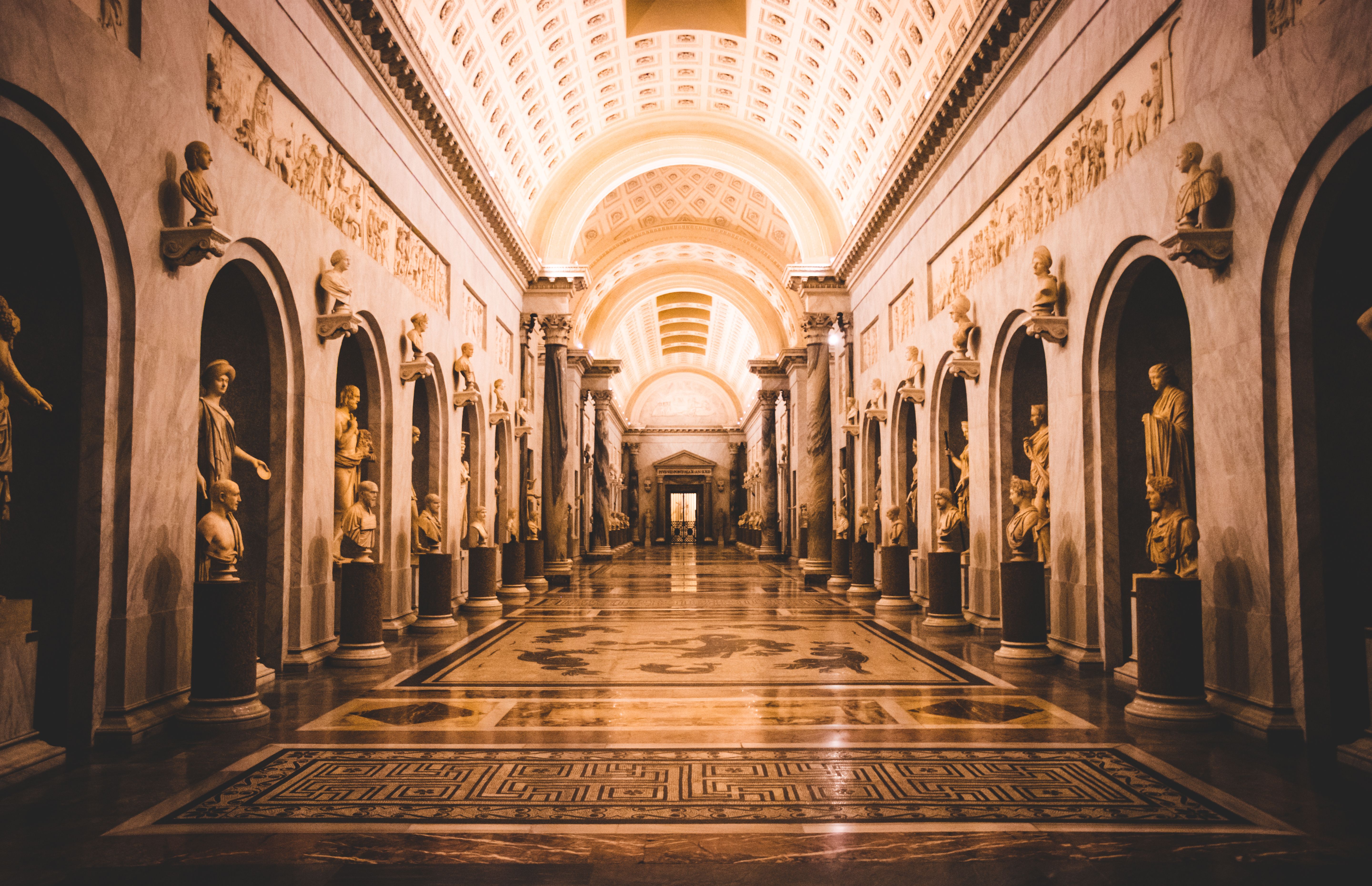 Visitors walking a hallway lined with classical sculptures in the Vatican Museums